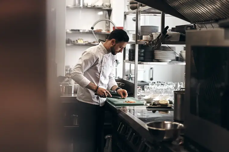 Un cuisinier prépare des légumes dans la cuisine d’un restaurant.
